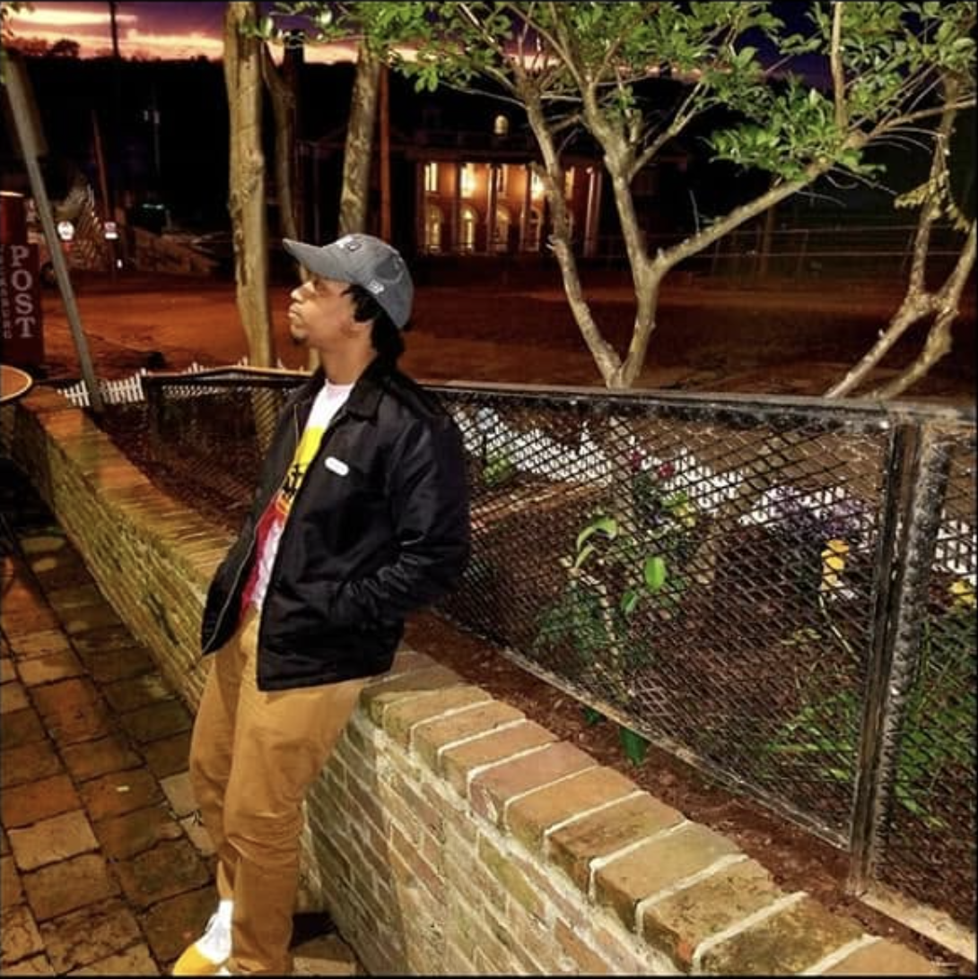 Sl1ck N°1 leaning against a wall at night